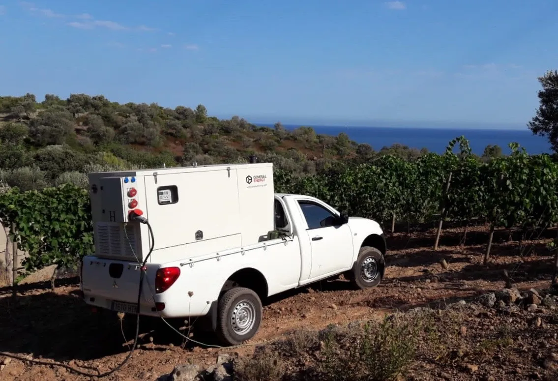 Camioneta de The Balearic Lighthouse con un generador insonorizado en la caja, aparcada en un viñedo frente al mar