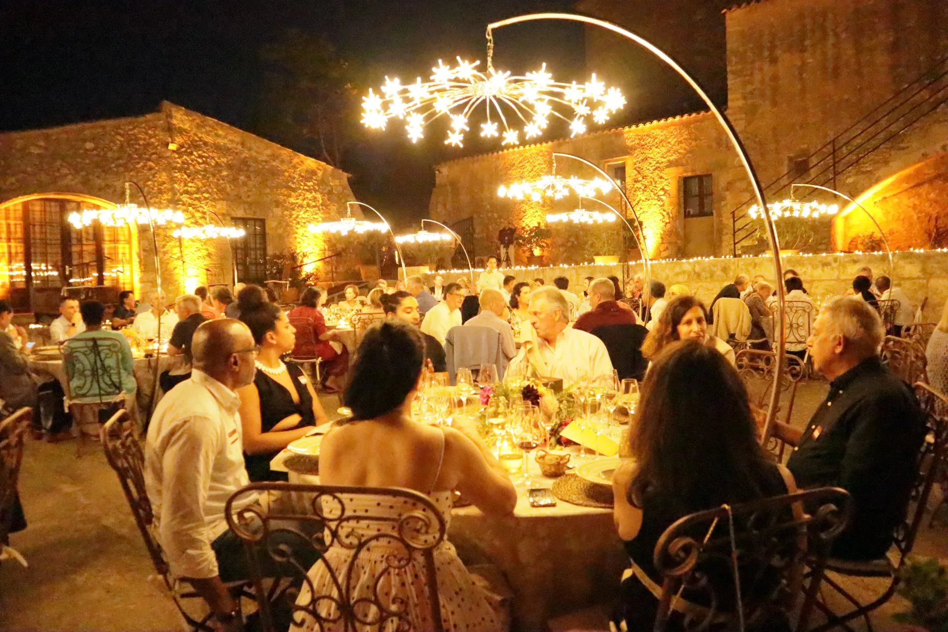 Cena de noche en el patio de una finca mallorquina, iluminada por una gran lámpara de araña suspendida de un báculo curvo